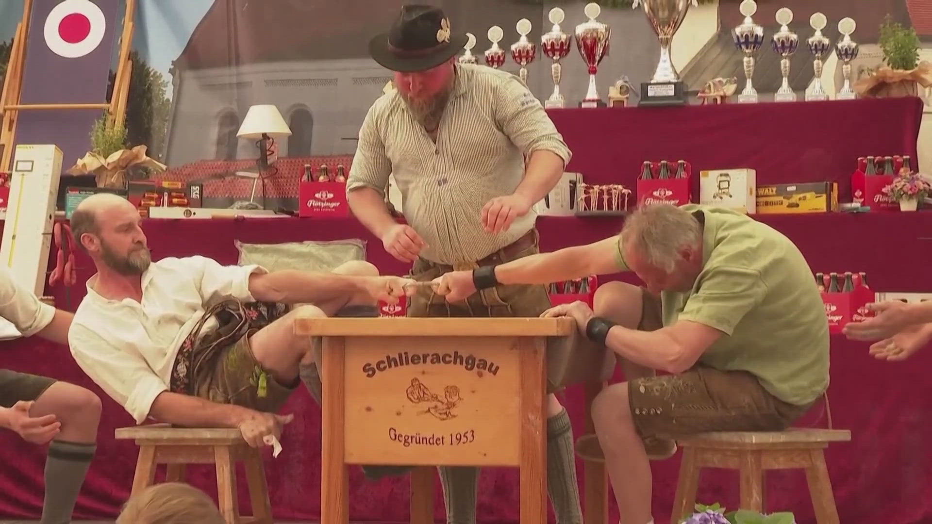 Men hook one finger through a small leather strap and try to pull the other person across the table. 