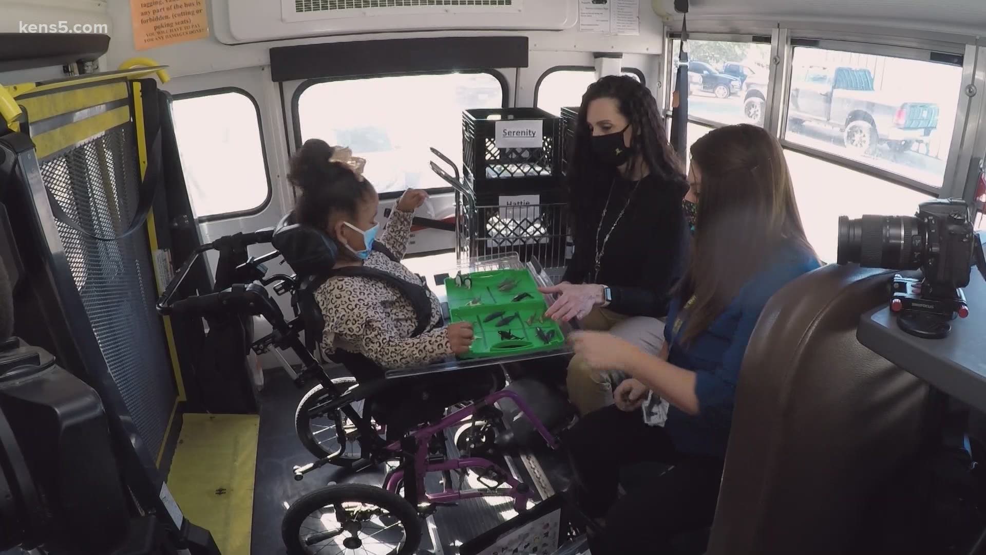 A special education teacher works with students one-on-one in the back of the bus that has been converted into a small classroom, wearing masks of course.